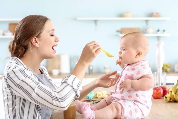 Mother feeding her little baby in kitchen at home - Фото, изображение