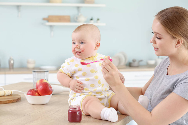 Mother feeding her little baby in kitchen at home - Photo, Image