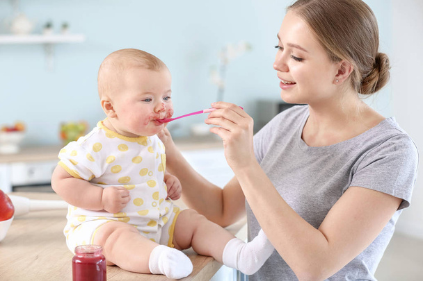 Mother feeding her little baby in kitchen at home - Foto, Imagen