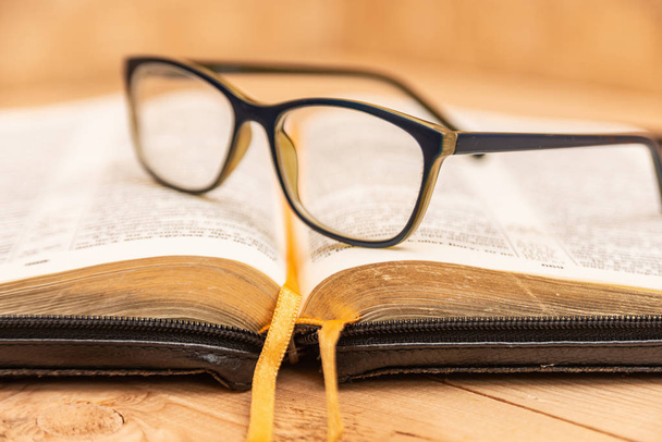 Gafas para la vista se encuentran en la Biblia, la Biblia en cuero negro cubierta con pestañas se encuentra sobre la mesa
. - Foto, Imagen