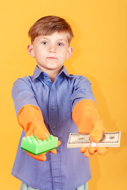 Przystojny chłopiec w niebieskiej koszulce i rękawice do mycia trzyma paczkę dolarów w jednej ręce i gąbki do mycia w drugiej i oferuje widzowi wybór. - Zdjęcie, obraz