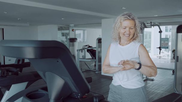 Seniorin treibt Sport auf einem Laufband im Fitnessstudio mit einer Sport-Cardio-Uhr - Foto, Bild