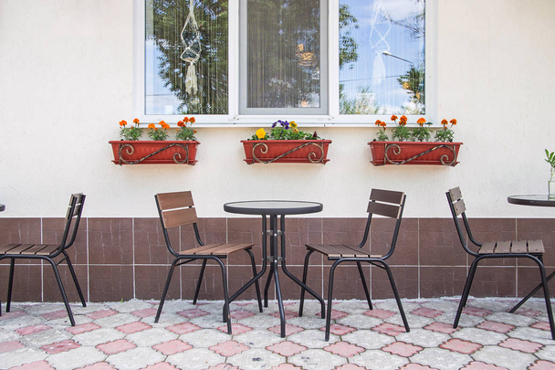 Szklane i metalowe stoły i krzesła na letnim tarasie kawiarni przy oknie z doniczkami kwiatów - Zdjęcie, obraz