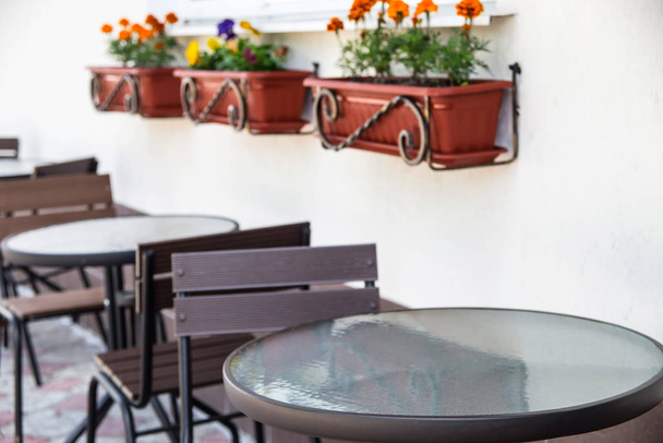 Skleněné a kovové stoly a židle na letní terase u okna s květináči květin - Fotografie, Obrázek