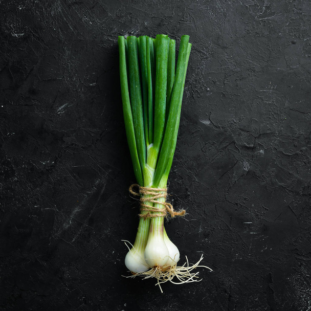 Fresh green onion on a black stone background. Fresh vegetables. Top view. Free space for text. - Foto, imagen