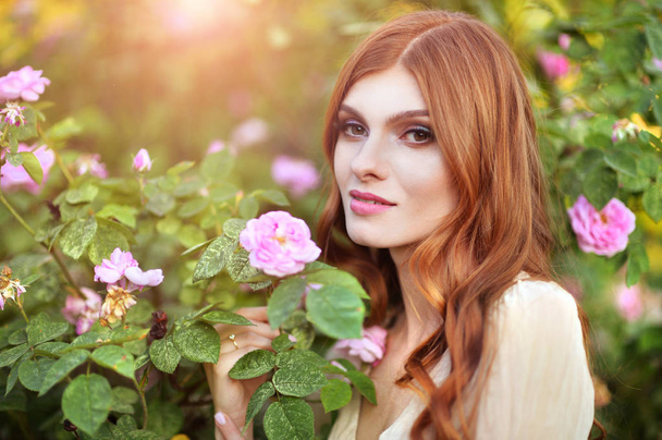 beautiful young woman  posing by rose bush  - Fotografie, Obrázek
