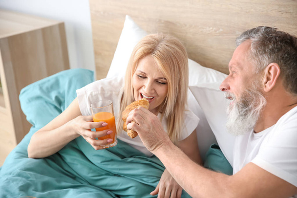 ベッドで朝食を食べる幸せな老夫婦 - 写真・画像