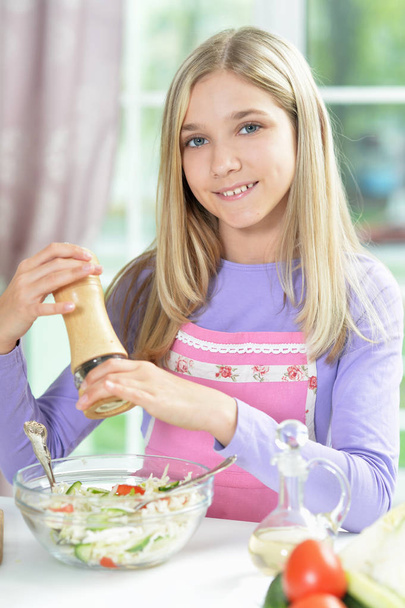 Cute little girl spicing fresh salad on kitchen table   - Photo, Image