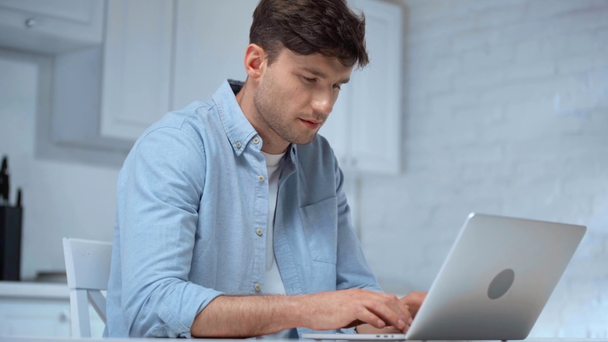 freelancer em camisa azul digitando no teclado do laptop e olhando para a câmera com suavemente sorriso na cozinha
 - Filmagem, Vídeo