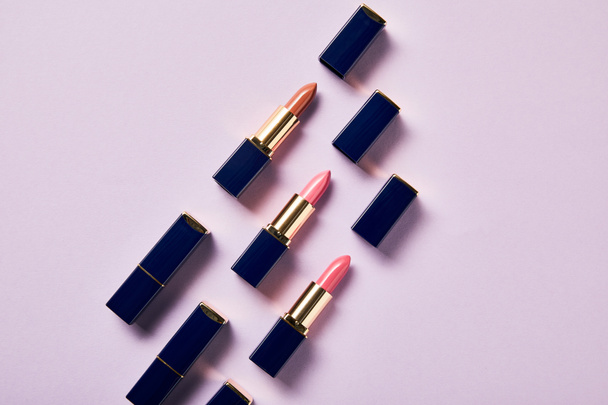 flat lay with various pink shades of lipsticks in tubes on purple    - Zdjęcie, obraz