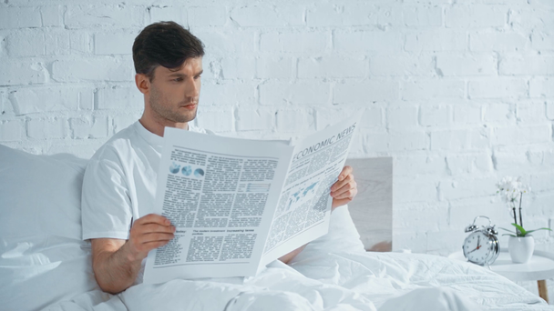 man in white t-shirt lying in bed, reading newspaper and turning pages - Footage, Video