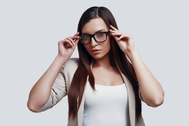 Taking close look. Attractive young woman looking at camera and adjusting eyewear while standing against grey background - Fotoğraf, Görsel