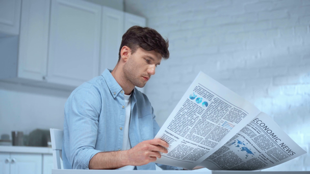gefocuste man in blauw t-shirt koffie drinken en een krant lezen in de ochtend in de keuken - Video