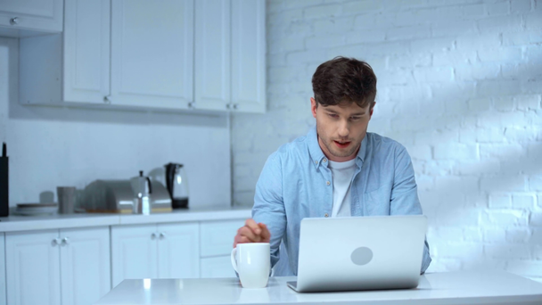Freelancer gieten koffie in beker, opening laptop, koffie drinken, typen op toetsenbord en zingen met glimlach - Video