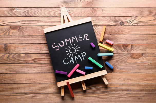 Chalkboard with text SUMMER CAMP and crayons on wooden table - Fotografie, Obrázek