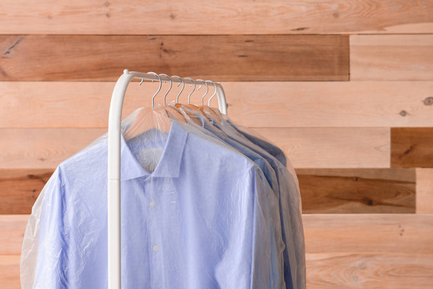 Stojan s oděvy po suchém čištění na dřevěné pozadí - Fotografie, Obrázek