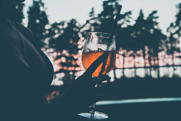 Ein Mädchen hält ein Glas mit einem Cocktail in der Hand. Das Bild wurde im Kurzentrum am Pool aufgenommen, vor dem Hintergrund des Sonnenuntergangs. - Foto, Bild