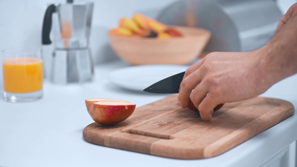 częściowy widok człowieka cięcia jabłko na drewnianej deski do krojenia i oddanie plastry na talerz w kuchni - Materiał filmowy, wideo