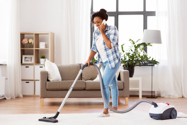 african american woman with vacuum cleaner at home - Fotó, kép