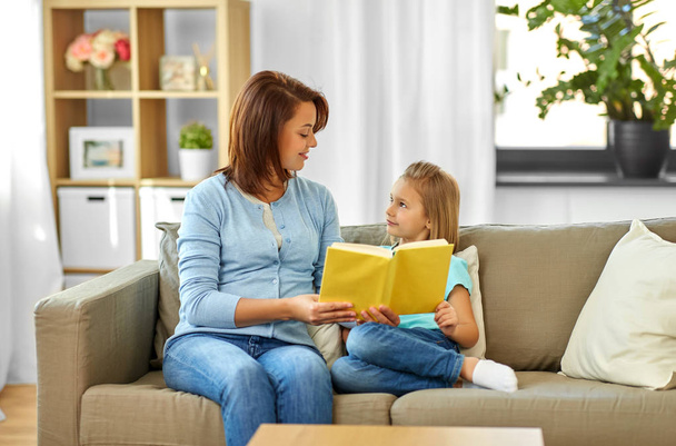 happy girl with mother reading book at home - Fotoğraf, Görsel