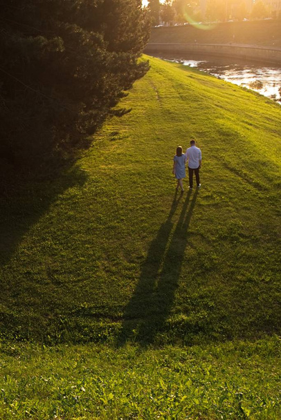 Jong paar loopt langs de oever van de rivier bij zonsondergang. - Foto, afbeelding