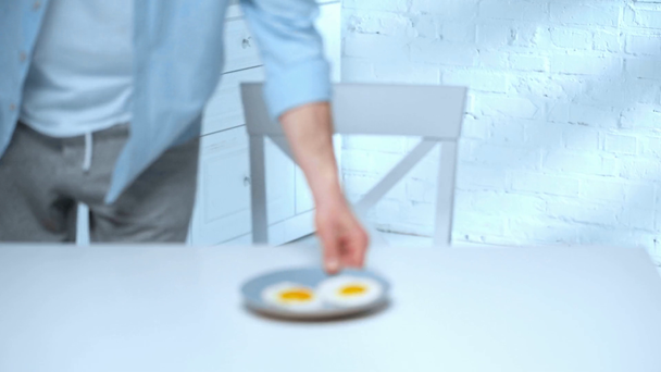 pulling focus of man holding plate with scrambled eggs, sitting at table and rubbing hands - Imágenes, Vídeo