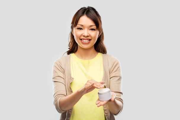 happy young asian woman holding jar of moisturizer - Фото, зображення