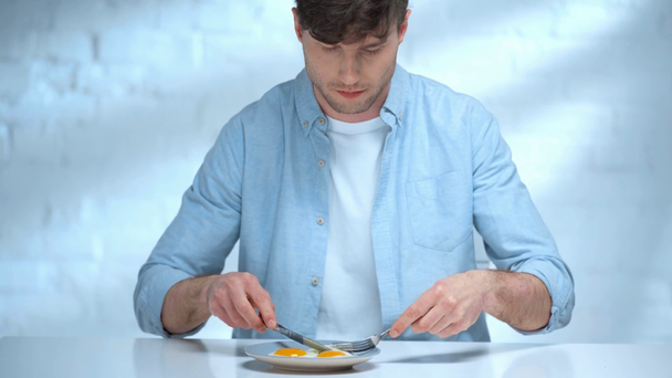 skoncentrowany człowiek za pomocą noża i widelca podczas jedzenia jajecznicę w kuchni - Materiał filmowy, wideo