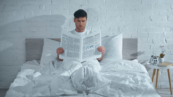 сосредоточенный мужчина в белой футболке лежит в постели и читает газету по утрам
 - Кадры, видео