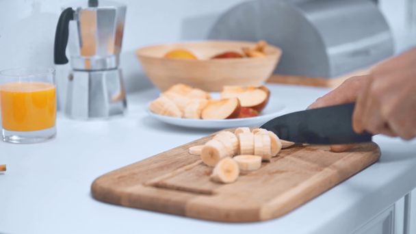 przycięte widok człowieka cięcia bananów na drewnianej deski do krojenia w kuchni - Materiał filmowy, wideo