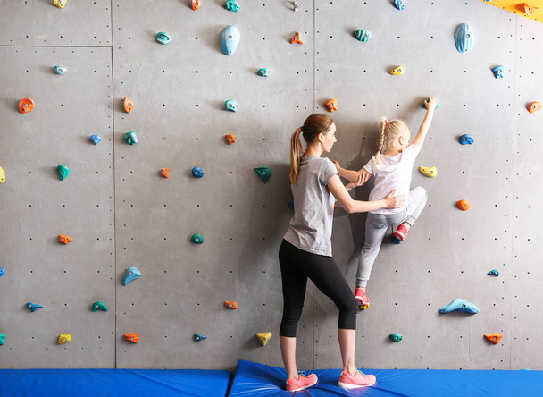 Ausbilder hilft kleinem Mädchen beim Klettern in Turnhalle - Foto, Bild