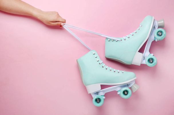 Vrouwelijke hand en vintage roller schaatsen op kleur achtergrond - Foto, afbeelding