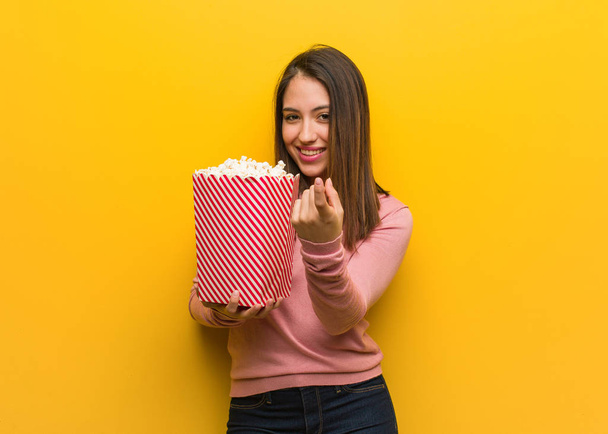 Young cute woman holding a popcorn bucket inviting to come - Photo, Image