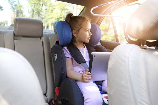 Klein meisje met Tablet computer geknikt in de auto veiligheid seat - Foto, afbeelding