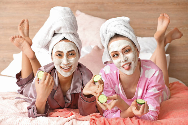 Όμορφες νεαρές γυναίκες με μάσκες προσώπου και φέτες αγγουριού στο σπίτι - Φωτογραφία, εικόνα