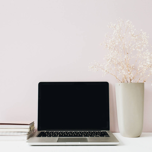 Scrivania minimalista per ufficio con laptop, mazzo di fiori su sfondo rosa. Intestazione eroe vista frontale con spazio di copia vuoto
. - Foto, immagini