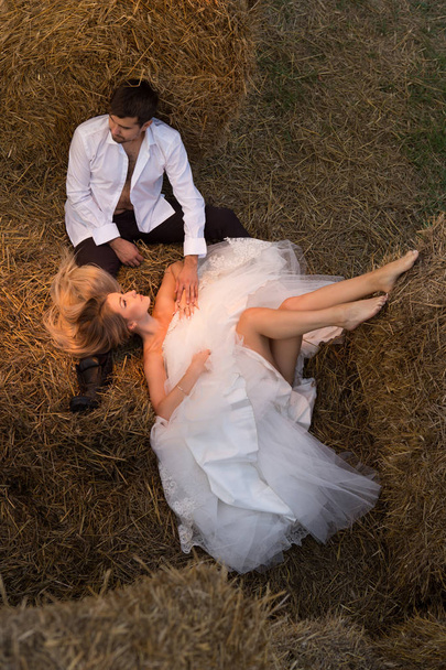 Groom strokes brides head while she lies on the hay - Foto, afbeelding