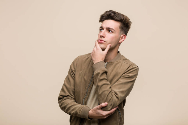 Jovem caucasiano vestindo uma jaqueta marrom olhando para os lados com expressão duvidosa e cética
. - Foto, Imagem