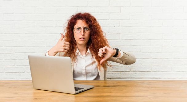 Young redhead curly woman working with her laptop showing thumbs up and thumbs down, difficult choose concept - Foto, immagini