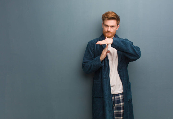 Young redhead man in pajama doing a timeout gesture - Фото, изображение