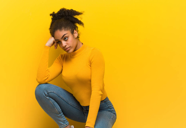 Young black woman sitting over an orange wall - Foto, immagini