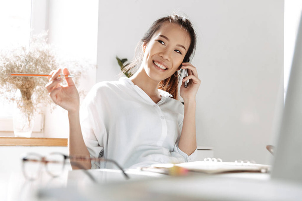 Happy asian business woman talking by smartphone and looking away - Photo, Image