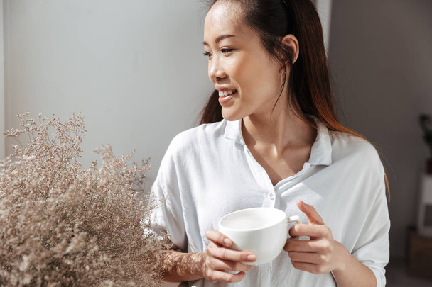 Щаслива азіатська бізнес-леді п'є каву і дивиться на вікно
 - Фото, зображення