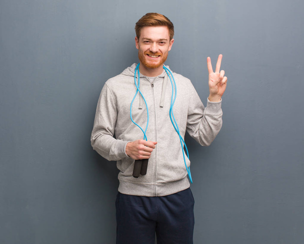 Young redhead fitness man showing number two. He is holding a jump rope. - Photo, Image