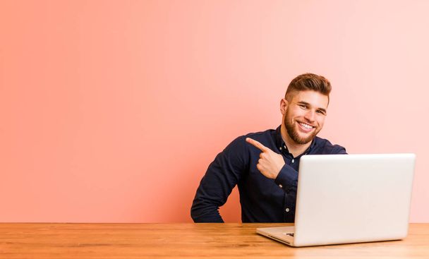 Dizüstü bilgisayarıyla çalışan genç adam gülümsüyor ve boş alanda bir şeyler gösteriyor.. - Fotoğraf, Görsel