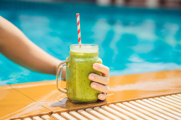 Woman with a green smoothies of spinach and banana on the background of the pool. Healthy food, healthy smoothies - Фото, зображення