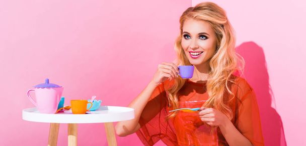 panoramic shot of beautiful smiling girl with toy cup on pink, doll concept - Fotó, kép
