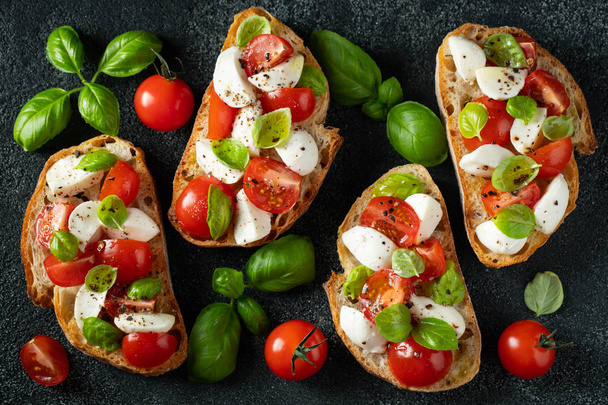 Bruschetta with tomatoes, mozzarella cheese and basil on a cutting board. Traditional italian appetizer or snack, antipasto. Top view with copy space. Flat lay - Photo, Image