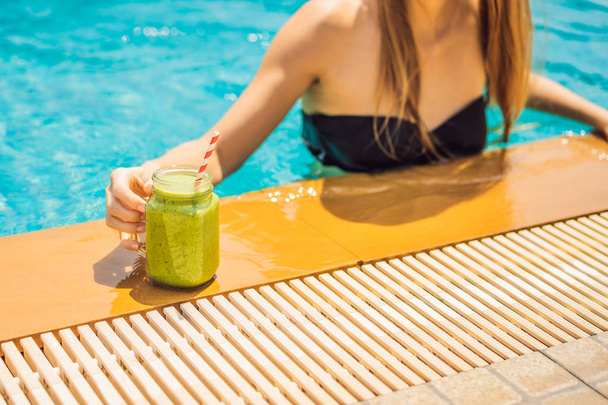 Woman with a green smoothies of spinach and banana on the background of the pool. Healthy food, healthy smoothies - Photo, Image