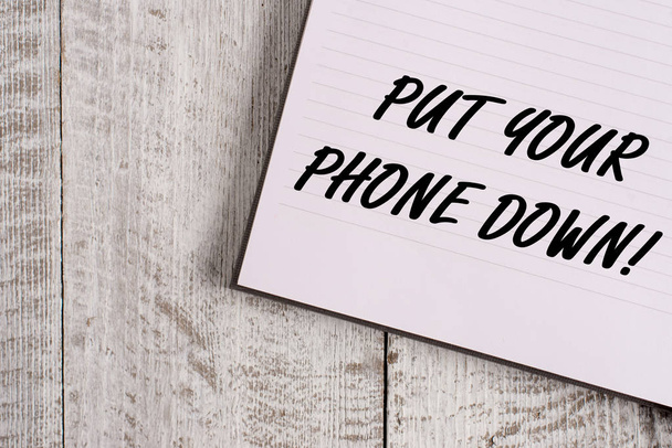 Conceptual hand writing showing Put Your Phone Down. Business photo showcasing end telephone connection saying goodbye caller Notebook stationary placed above classic wooden backdrop. - Photo, Image